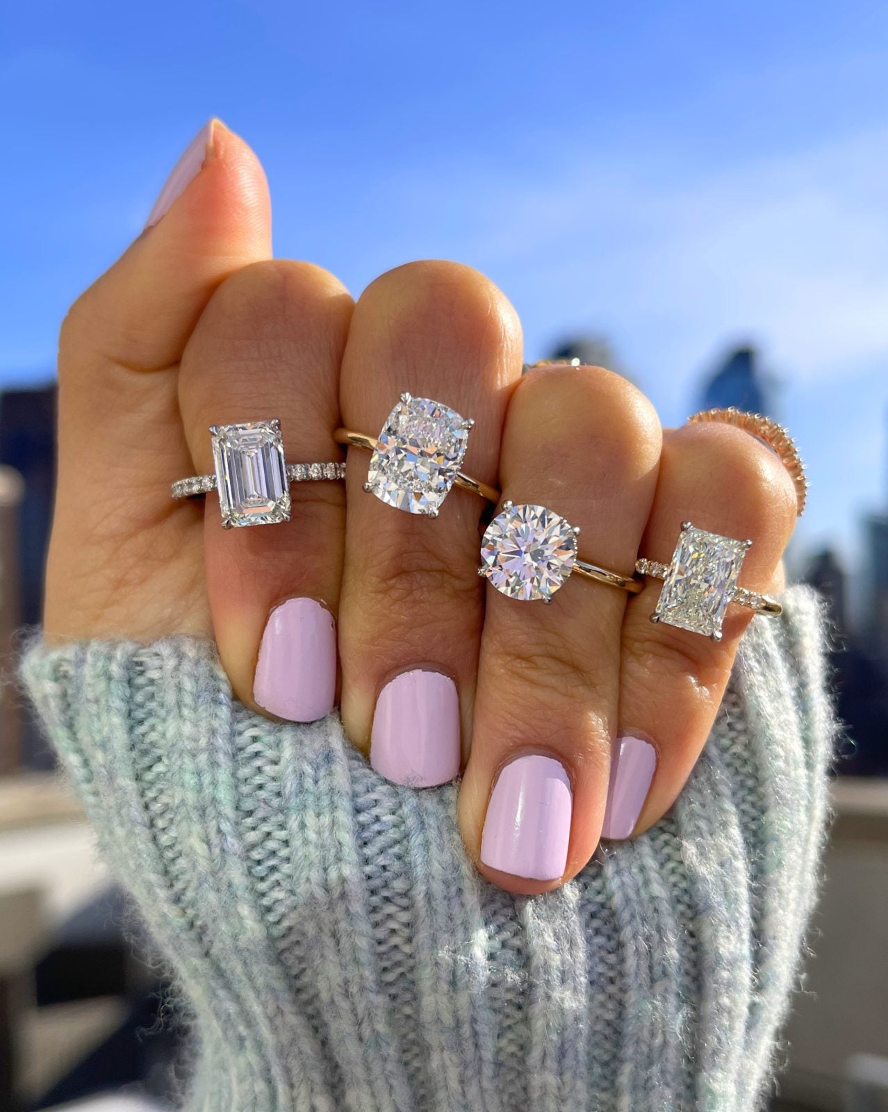 A hand wearing four engagement rings against a city skyline