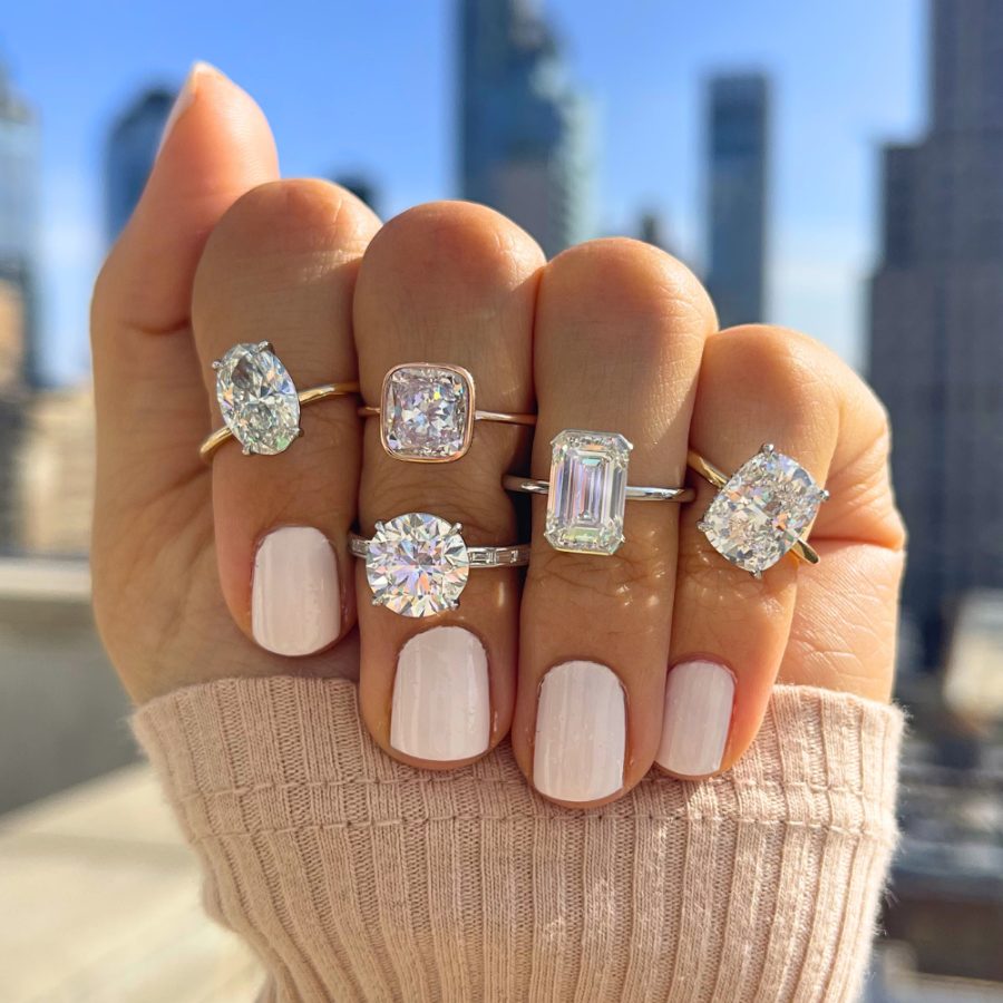 A hand wearing several diamond engagement rings against the New York City skyline