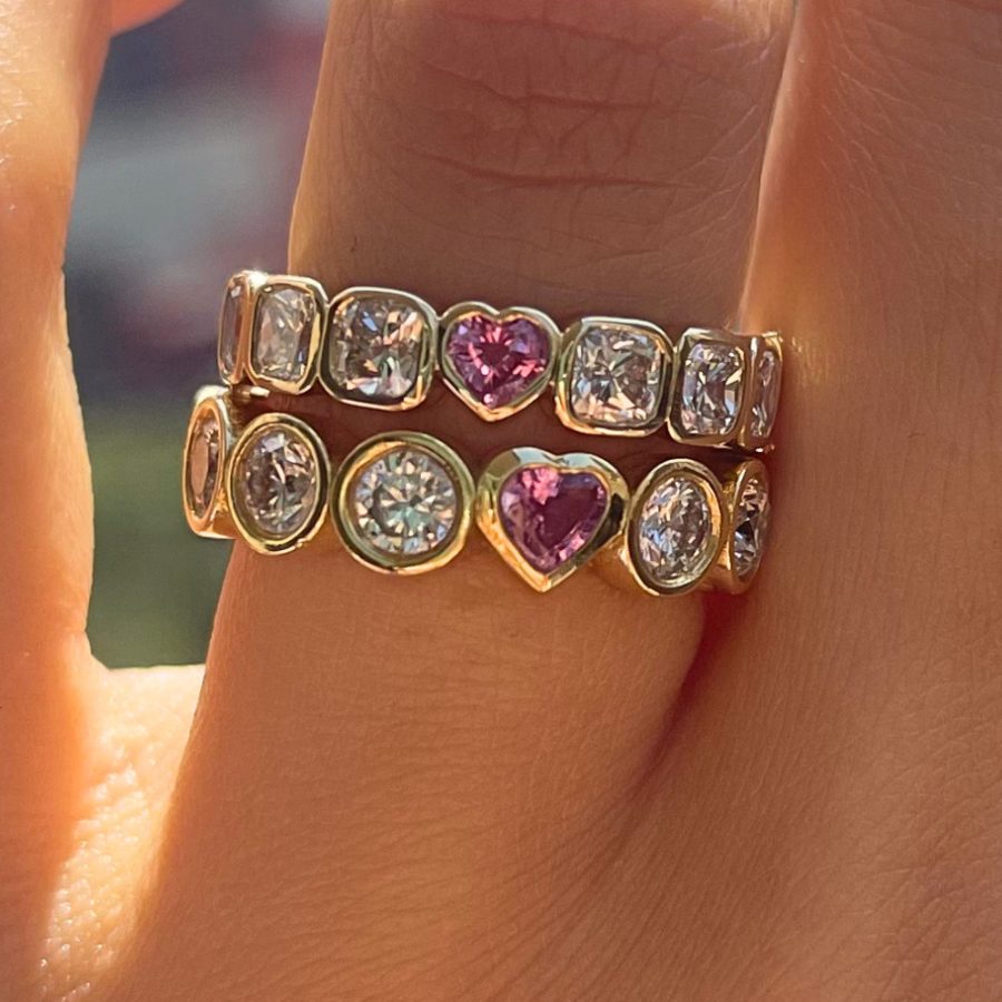 Two stacked gold bezel-set eternity bands of diamonds with a pink heart-shaped gemstone